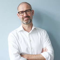Dr. med. Draeger steht vor einer blaugrauen Wand